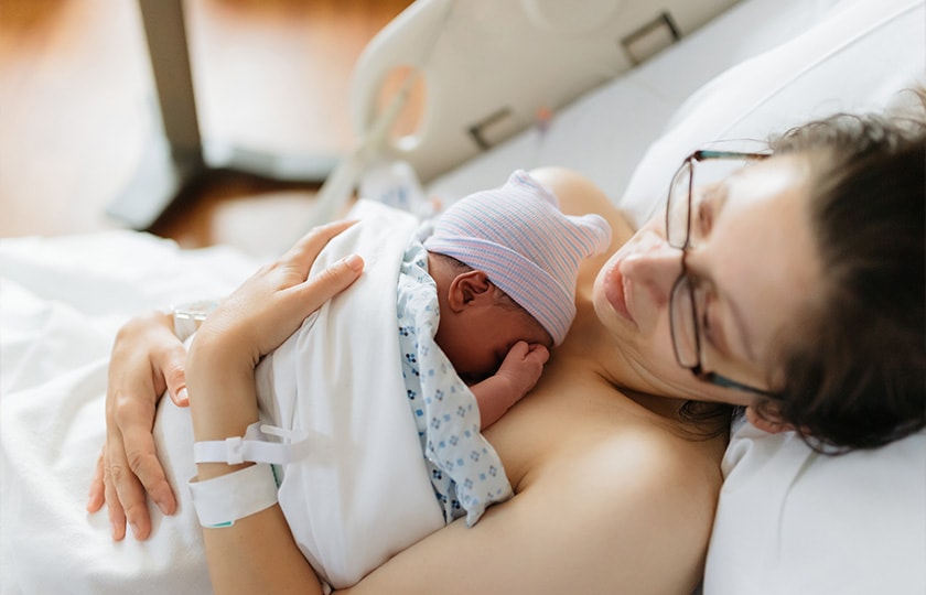 Mother embracing baby on hospital bed.