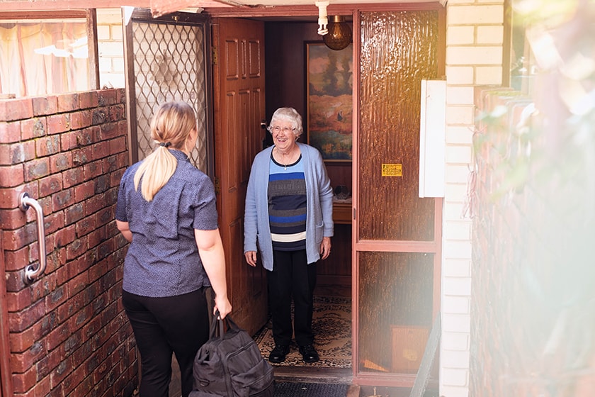 An elderly lady greets a visiting nurse at the door