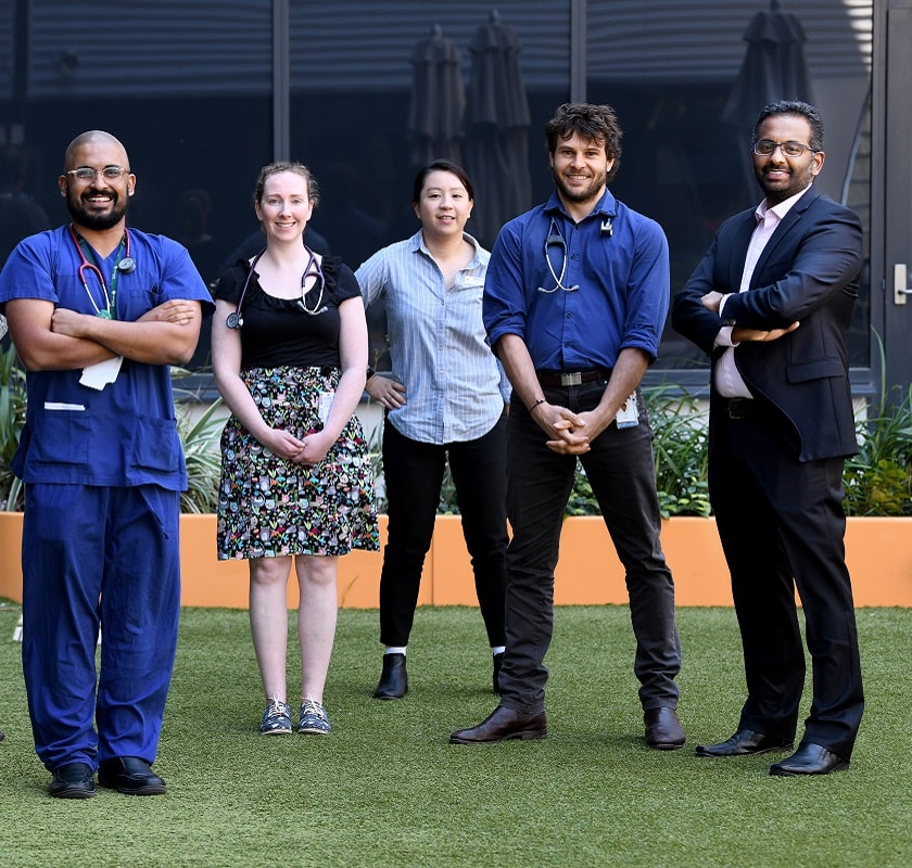 Group of seven health professionals of different races and genders standing side by side in a courtyard