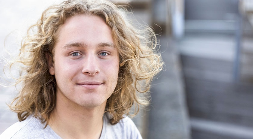 Portrait of young man with long curly hair, background with copy space, full frame horizontal composition