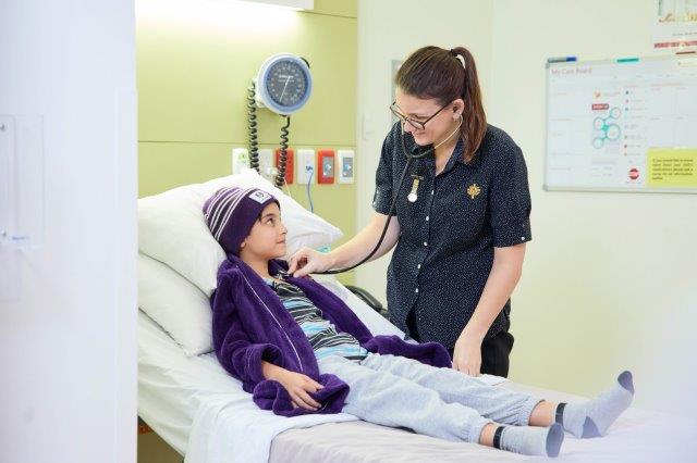 Child in bed receiving treatment from caregiver.