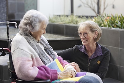 Patient sitting in wheelchair smiling and talking with caregiver