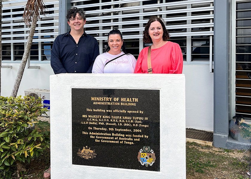Dr Haydn Aarons, Nicole Ford, and Carolyn Mornane stand in front of a building and behind a sign that reads Ministry of Health Administration Building.