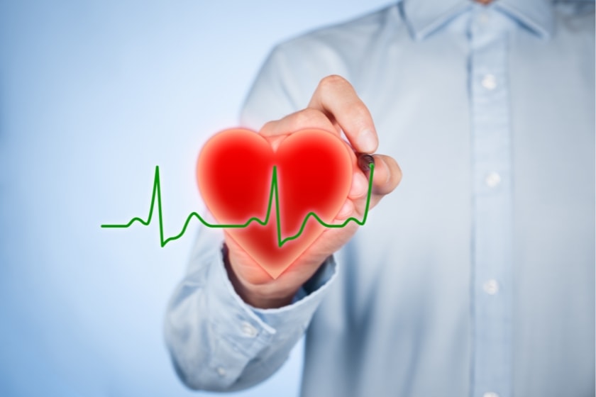 Person in a light blue shirt holding a glowing red heart graphic with a green ECG heartbeat line overlaid, symbolising cardiology or heart health.
