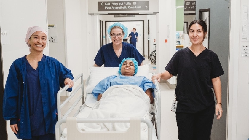 Three caregivers accompany a patient in a bed going down a hospital hallway.