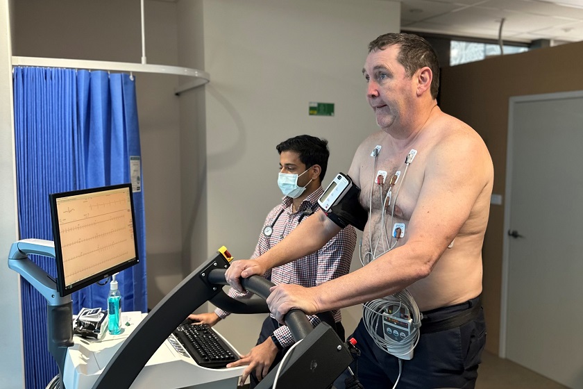 A man on a treadmill doing a stress echocardiogram while a specialist observes a computer monitor.