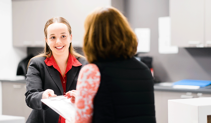 Caregiver greeting patient at reception and handing them admissions information
