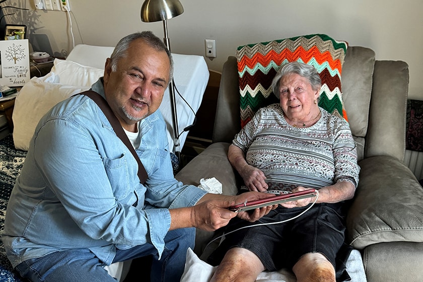 Jeremy Stork holding an iPad while his mother-in-law Pat sits in a lounge chair, both looking at the camera.