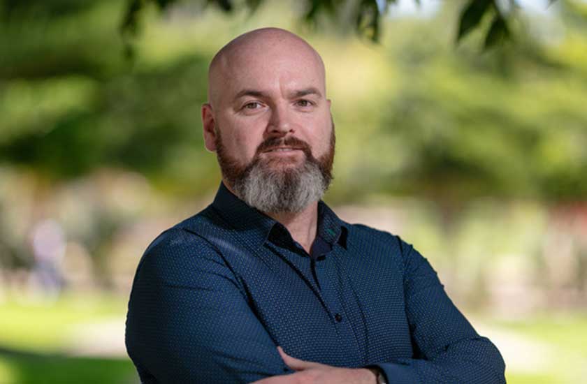 Dr Cam McLaren smiles into the camera with his arms folded 