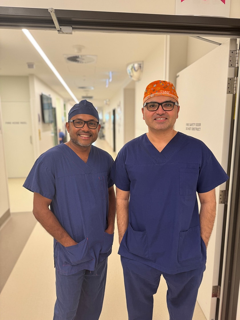 Gynaecologist Dr Saj Rathnayake and Colorectal Surgeon Mr Hanumant Chouhan stand next to each other in surgical scrubs smiling