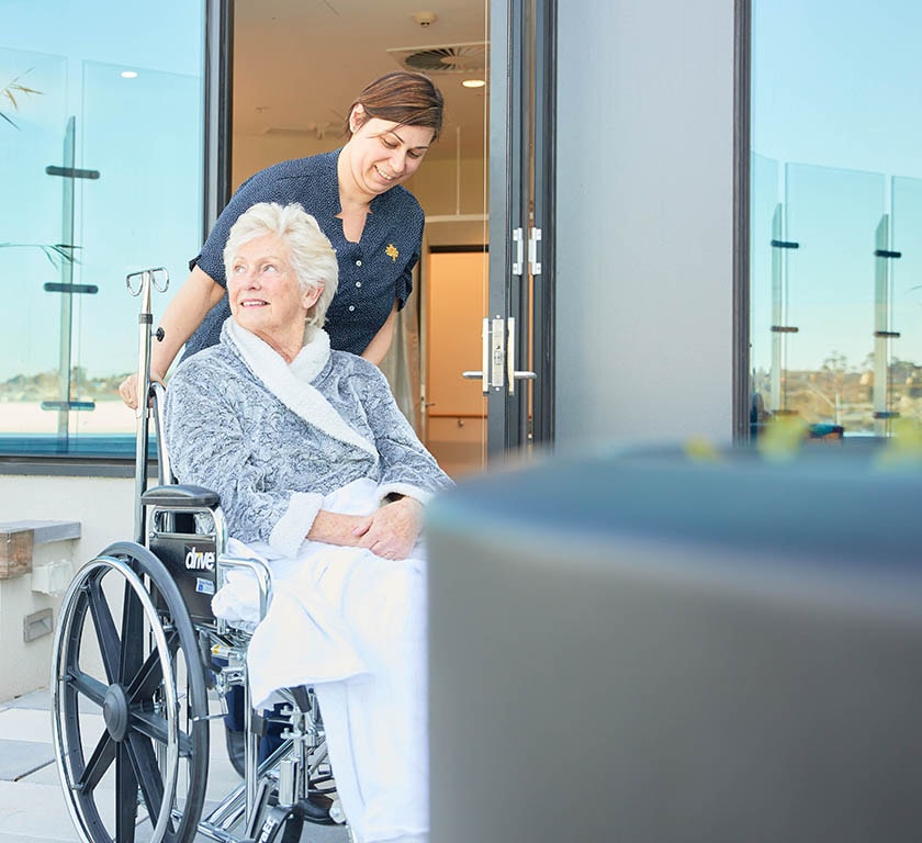 Caregiver pushing patient in wheelchair outside of hospital