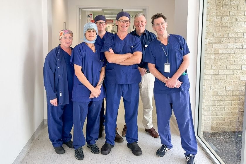 Caregivers standing in a hallway wearing blue scrubs, smiling at the camera.