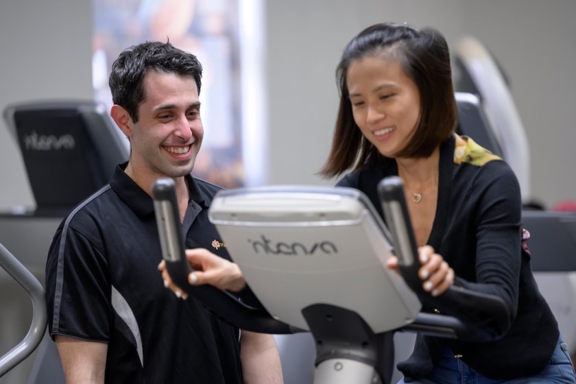 Caregiver Adrian Meli assisting a patient on an exercise bike.