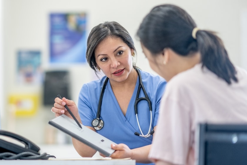 A female doctor with a stethoscope around her neck shows a paper to a female patient