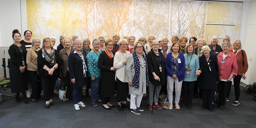 A large group of people standing in front of a leafy backdrop, smiling at the camera.