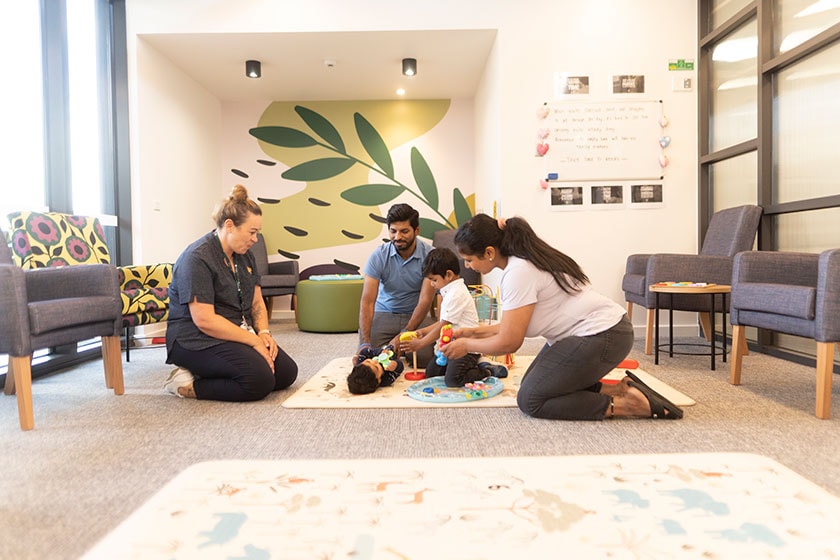 Caregivers with parents and infant on a padded mat on the floor in the communal living space