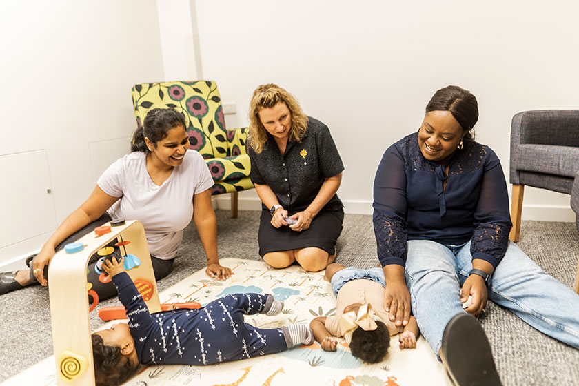 Caregiver with mothers and babies on a padded mat on the floor with toys