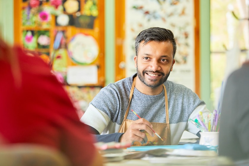 A person wearing an art apron, painting in a colourful art room.