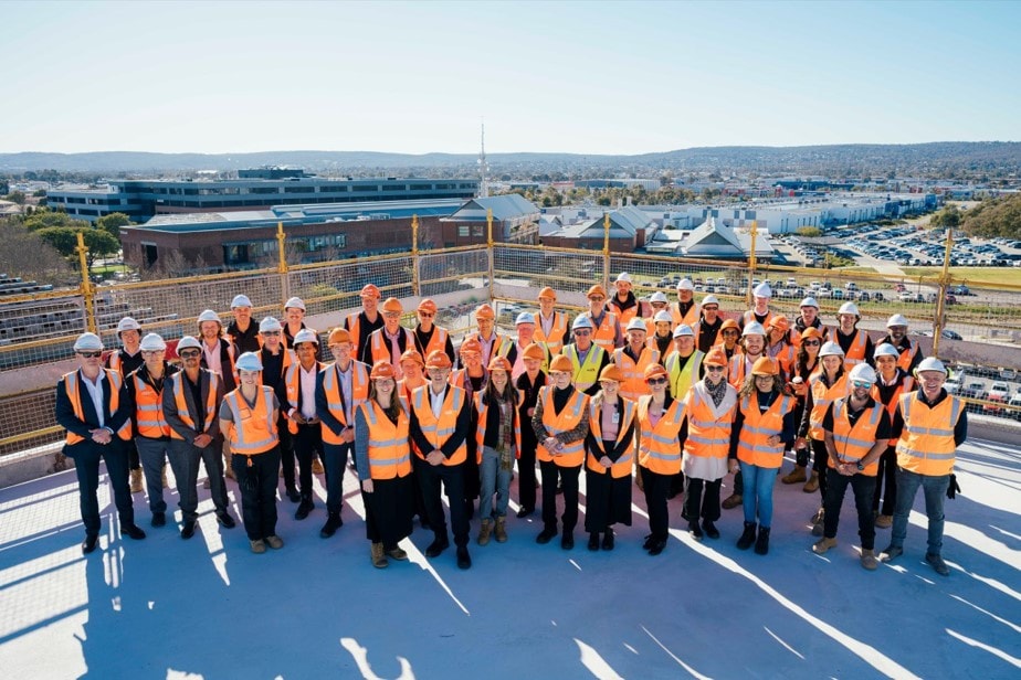 People wearing orange hi-vis vests standing on top of the roof of the topped-out St John of God Midland Private Hospital.