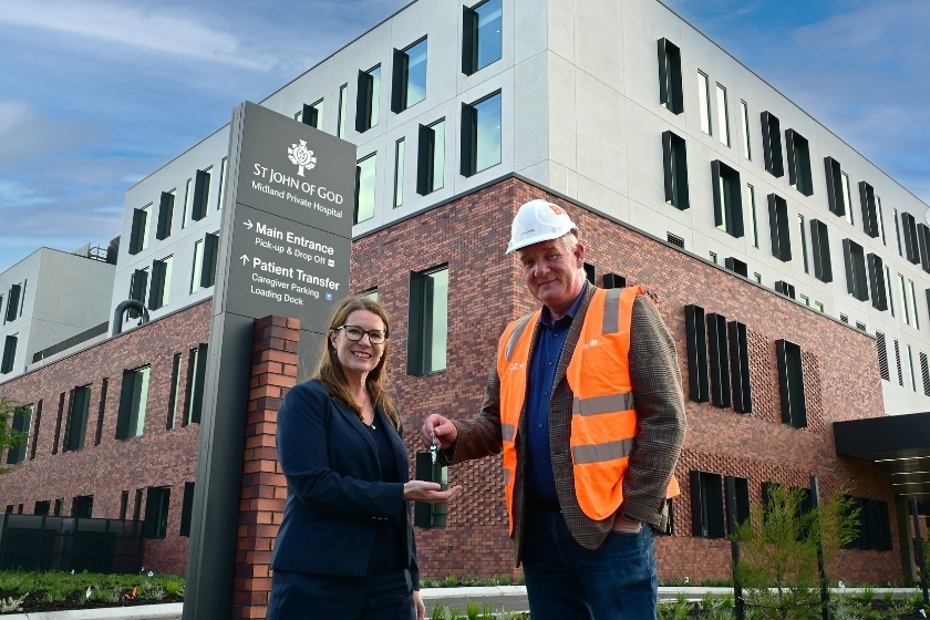 Handover of keys from a person in a construction outfit to a person in a corporate outfit, with in the background the new Midland Private Hospital