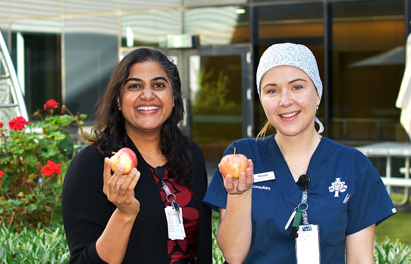 Caregivers holding apples outside of the hospital for Bowel Cancer Awareness Month
