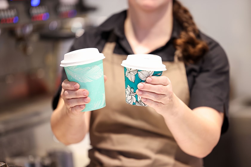 A person holding two take-away coffee cups.