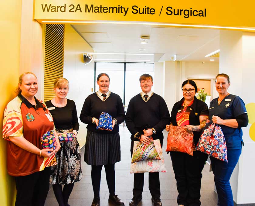 Students from Guildford Grammar School and caregivers smile holding the gifted toiletry bags