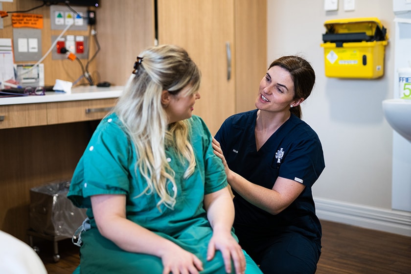 Pregnant maternity patient in patient room setting sitting upright with midwife assisting to her side
