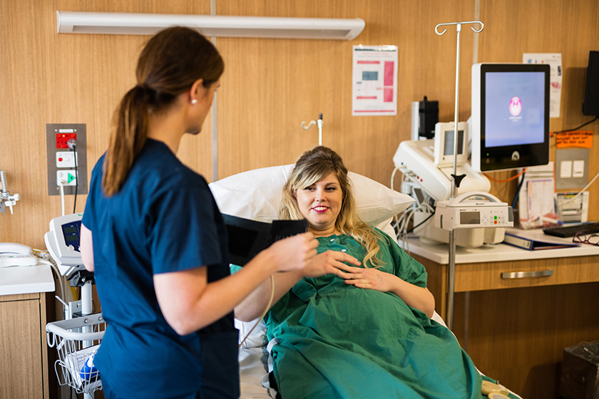 Pregnant maternity patient lying in bed in a patient room with midwife bedside stretching out the cuff of the blood pressure machine