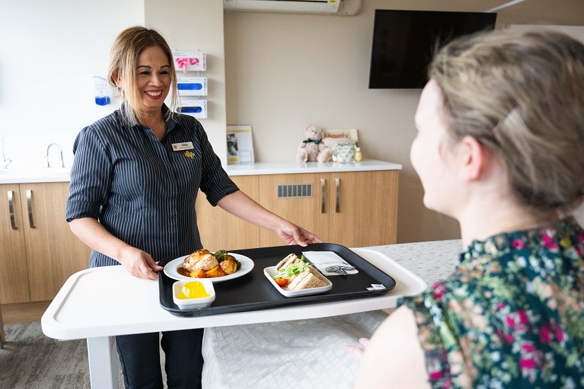 Caregiver serving meal tray to a patient at their bedside