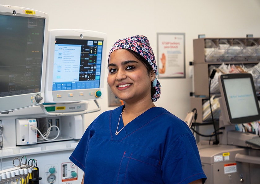 Registered Nurse Nicole Lobo pictured in surgical scrubs by medical monitoring equipment.