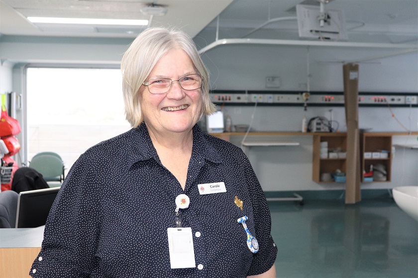 Nurse in uniform smiling and standing in a clinical area