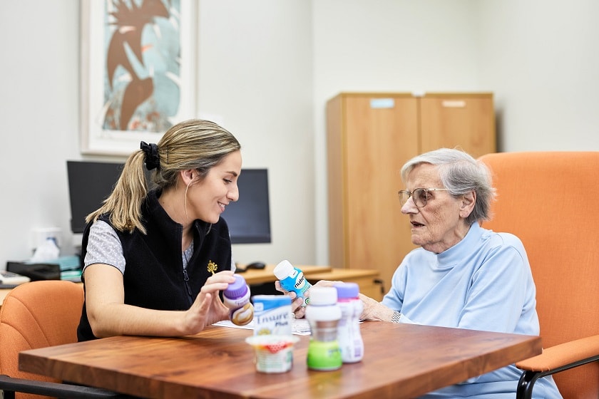 Dietitian seated with an elderly female patient discussing feeds.