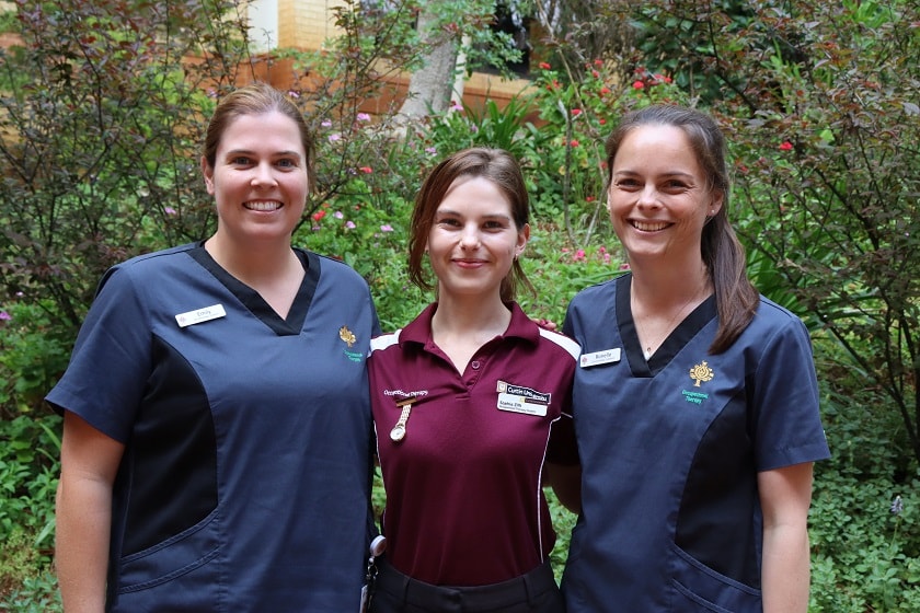 Three people standing in a garden, smiling at the camera.