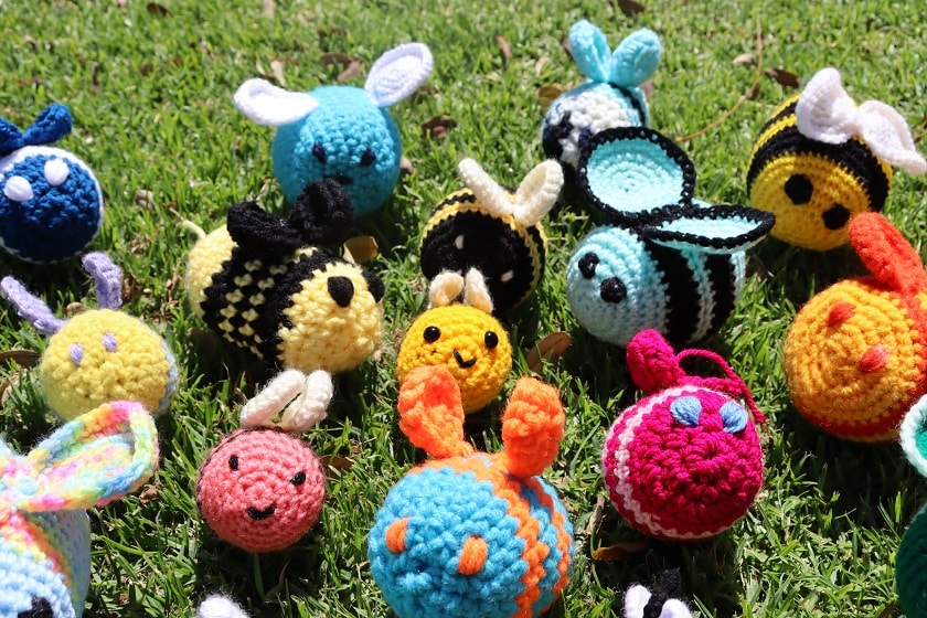 An assortment of knitted, stuffed bees laying on grass.