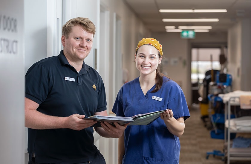 Two caregivers standing in a ward corridor both holding a folder 