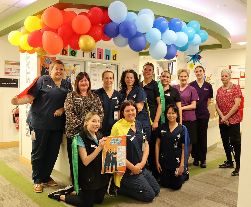 Caregivers from the St Rose Thrive Ward Council smile at the camera in front of a desk, with colourful balloons hanging from the ceiling.