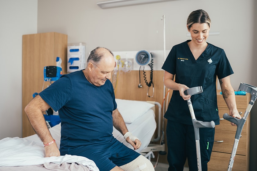 A caregiver assists a patient getting out of bed by holding his crutches