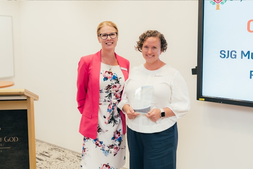 2 people posing in front of a whiteboard in an award ceremony, the person in the right is holding a glass trophy 