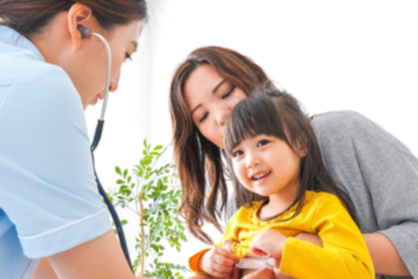 a mom is holding her daughter on her lap while a medical professional checks her lungs with a stethoscope 