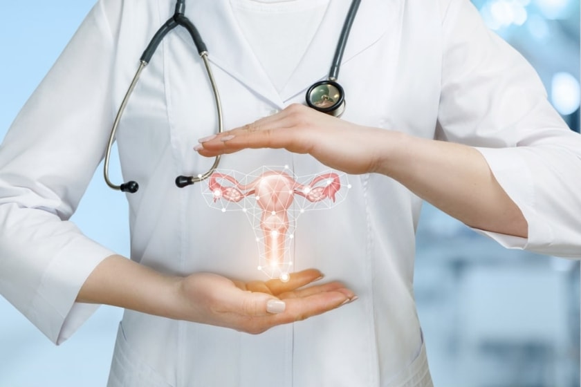 Healthcare professional in a white coat with a stethoscope, holding a glowing digital illustration of a uterus between their hands, symbolising women’s reproductive health and gynecological care.