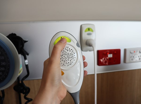A hand holding a call bell and pressing on the button in a hospital room