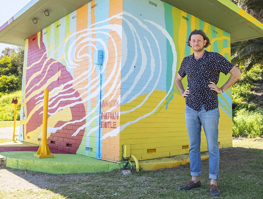 Artist Nathan Hoyle posing before one of the building he painted