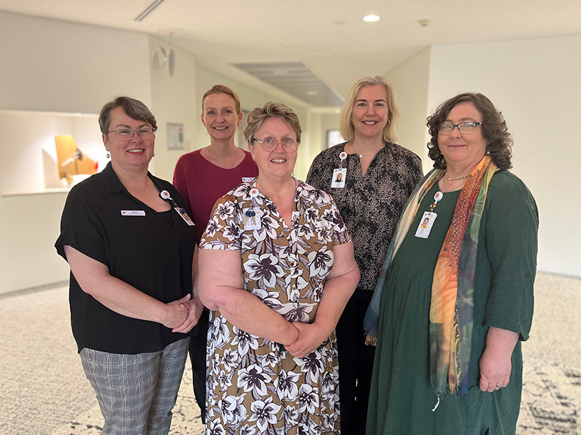 Members of St John of God Subiaco Hospital's pastoral services team sitting and standing in a room, smiling at the camera.