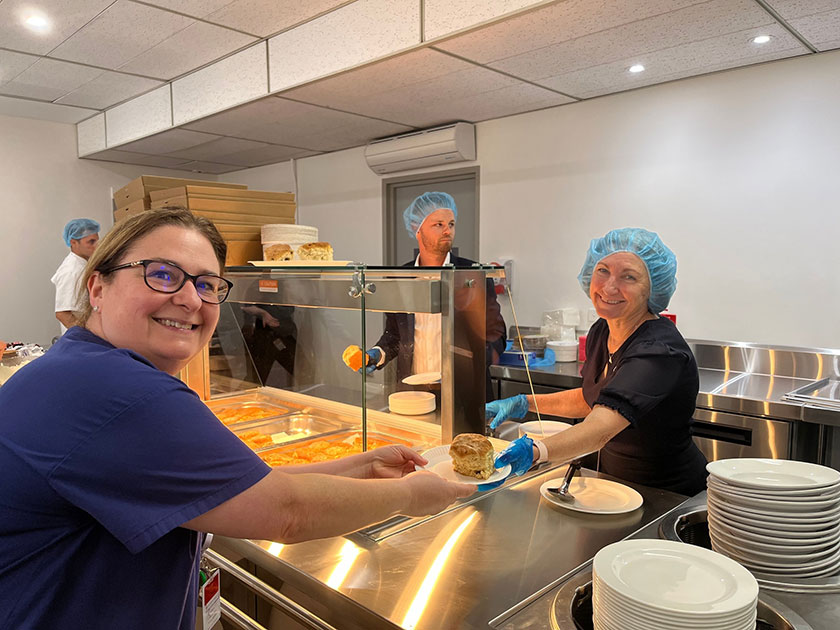 Cafeteria lady smiling as she hands nurse a scone