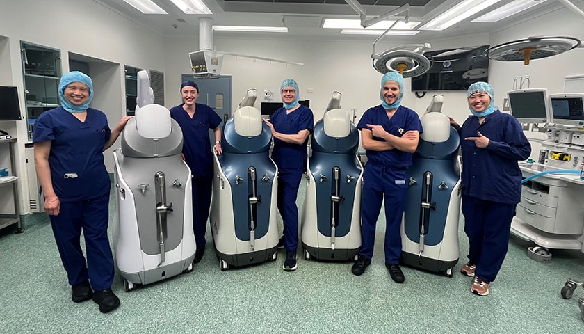 Caregivers wearing scrubs in an operating theatre, with four Mako robots.