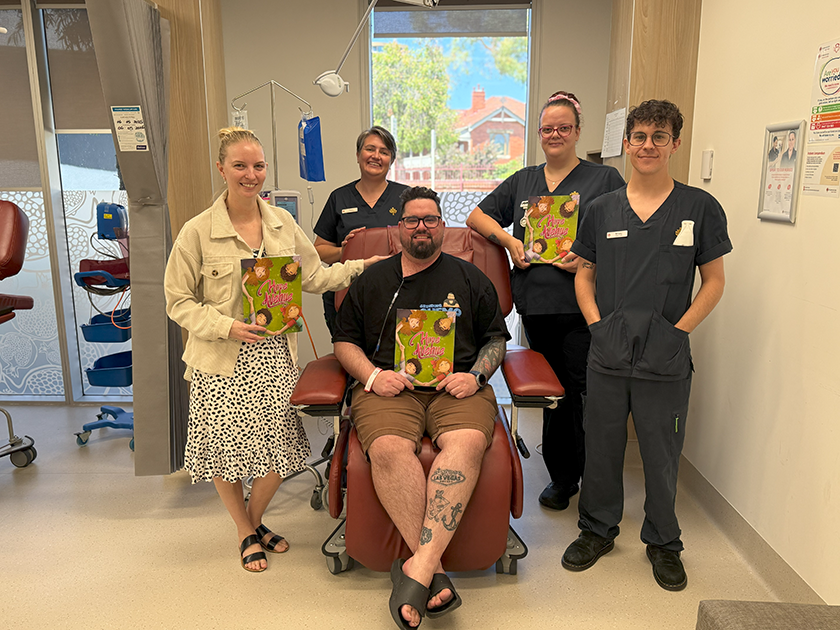 A patient sitting in a chair, surrounded by 3 medical professionals wearing dark blue scrubs and 1 person in normal clothing. Three of them are holding a book with a green cover.