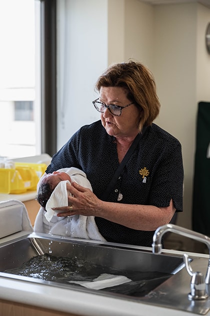 A caregiver washing a newborn baby's head over a hospital bathing sink.