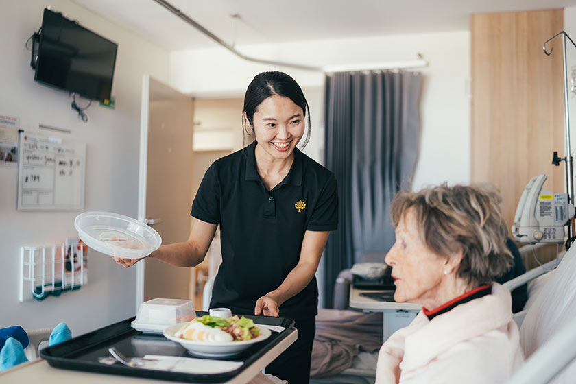 A caregiver serves a patient a fresh caesar salad in bed.