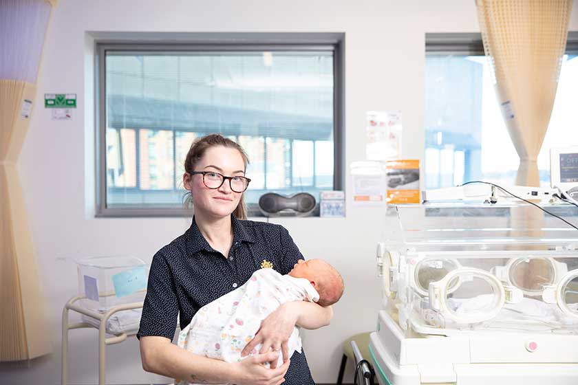 Midwifery caregiver holding a baby in their arms in hospital room